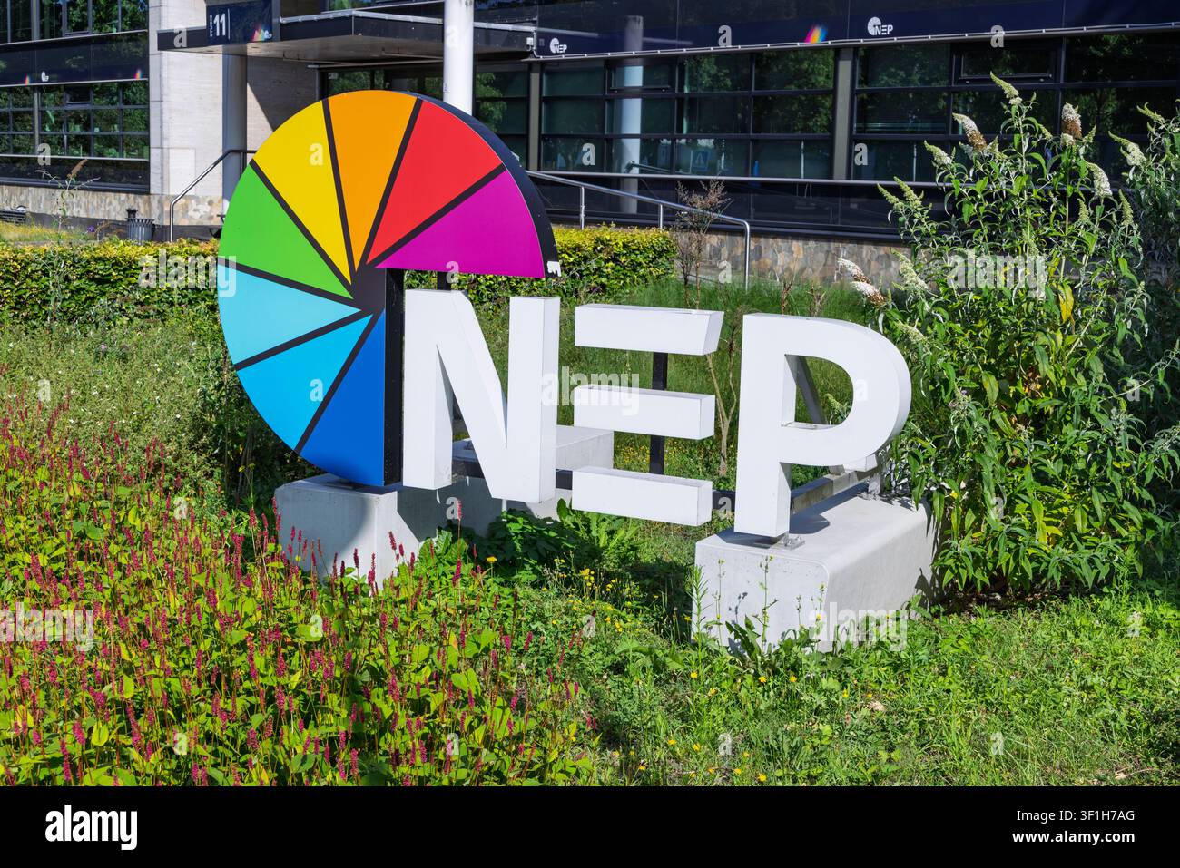 Hilversum, Paesi Bassi - 13 luglio 2026: Le lettere bianche e il logo a ruota multicolore di NEP Group, un'azienda globale di tecnologie mediatiche, posizionati in un gar Foto Stock