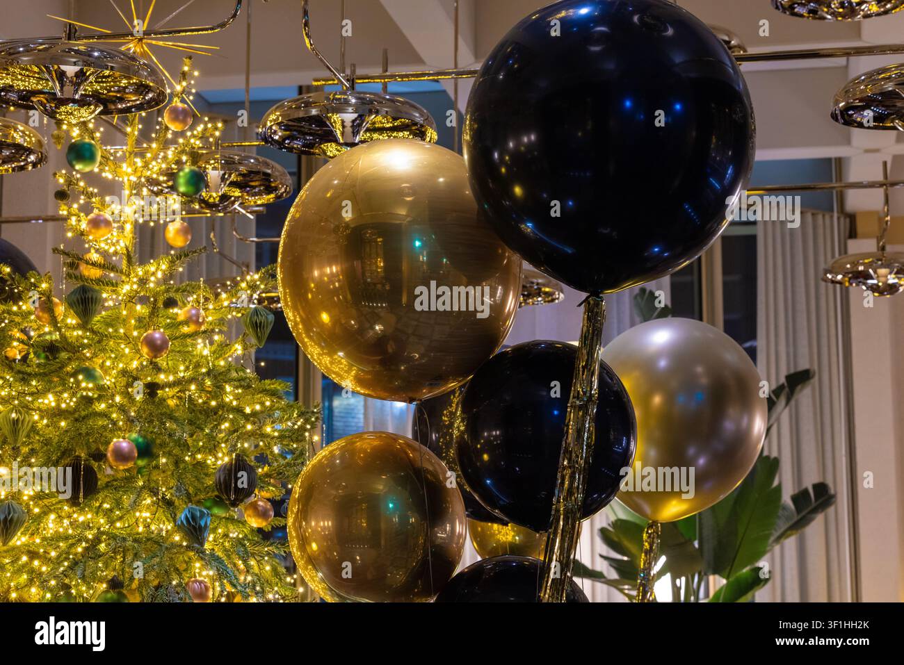 Esposizione elegante per le feste con palloncini a sfera neri e dorati lucidi accanto a un albero di Natale illuminato a festa. Foto Stock