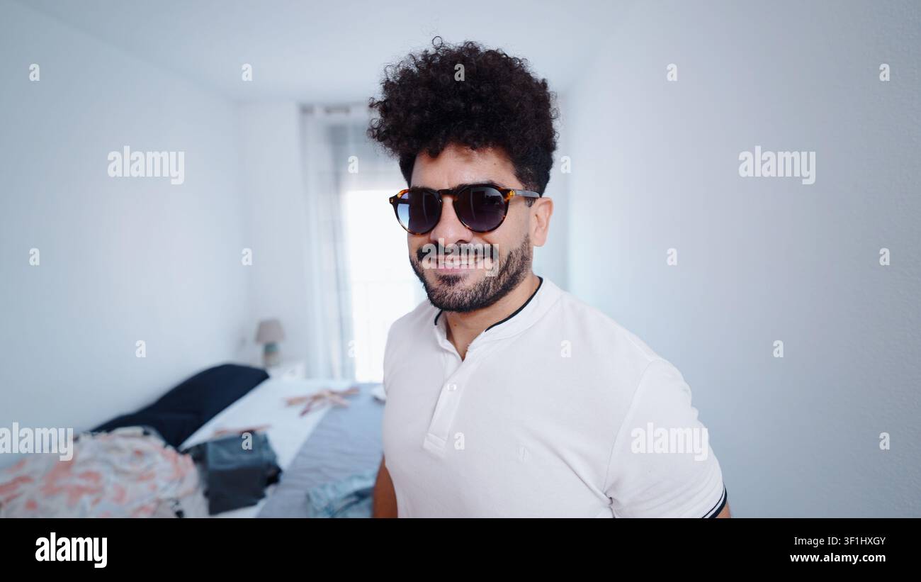 Uomo elegante con occhiali da sole che sorride, impacchettando vestiti per un viaggio a casa Foto Stock