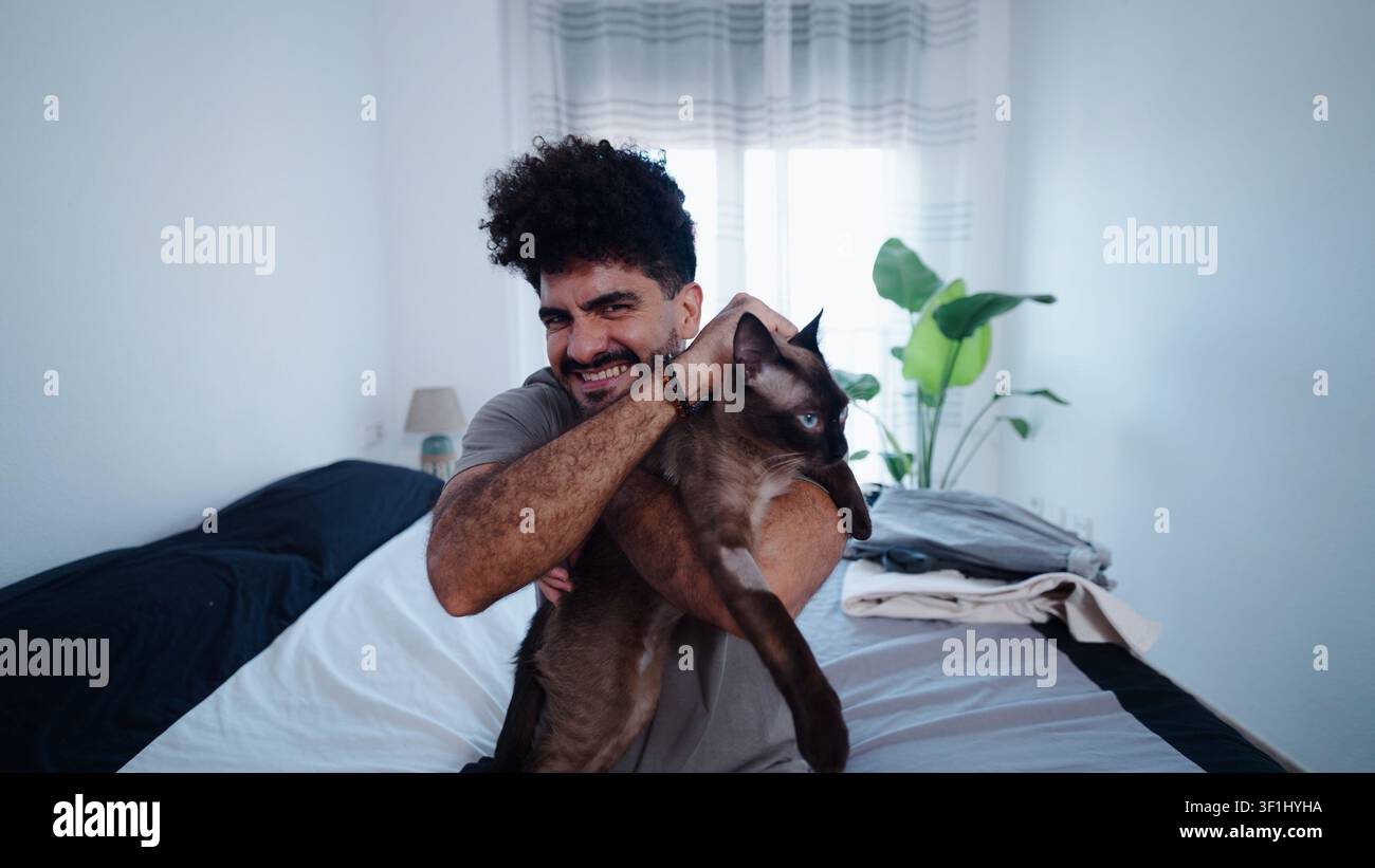 Uomo felice che tiene il suo gatto, godendosi la compagnia degli animali domestici a casa Foto Stock