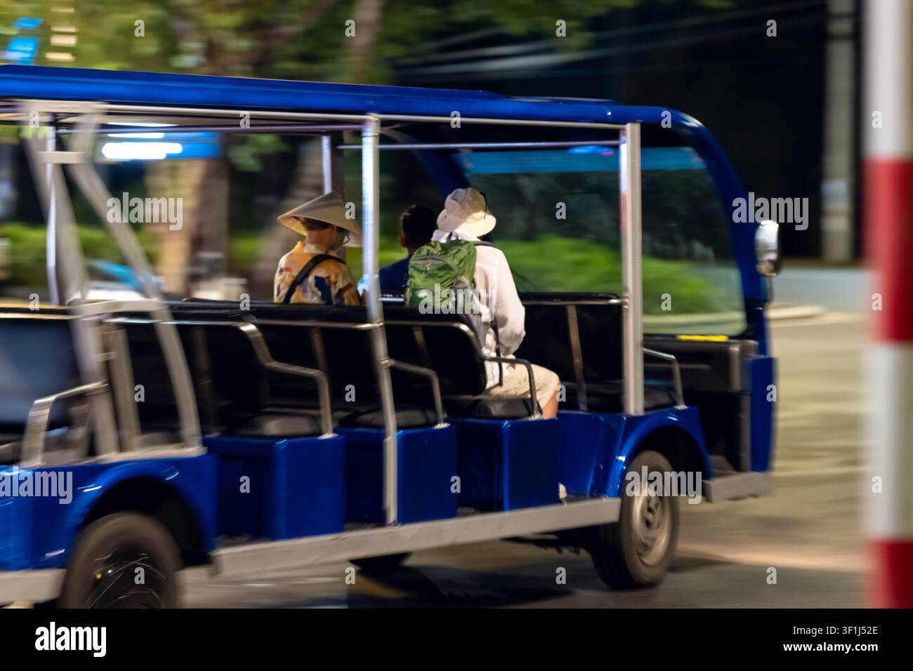 Piccolo shuttle blu aperto che guida di notte con tre passeggeri che indossano cappelli distintivi Foto Stock