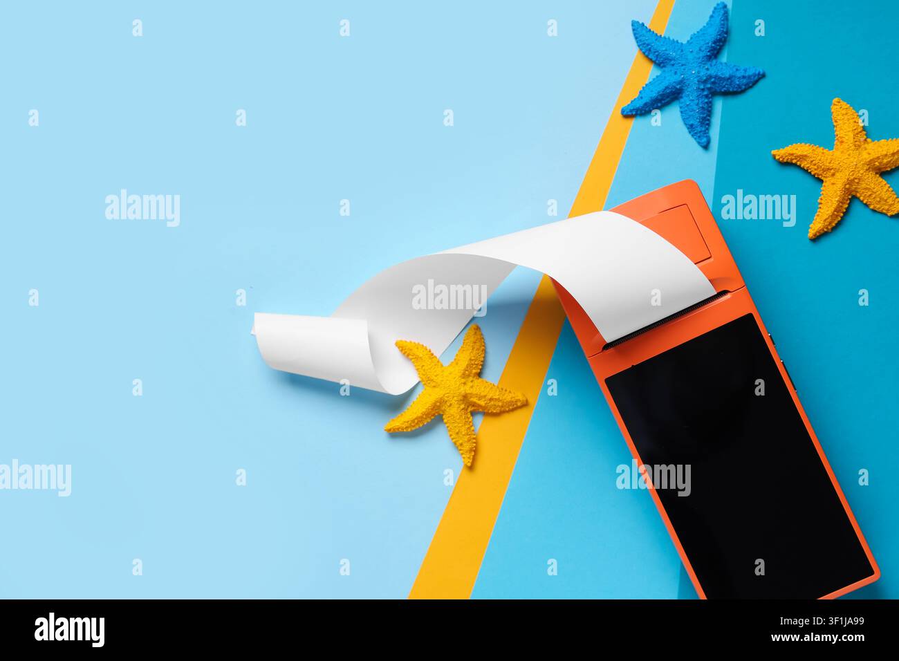 Terminal di vendita a punti arancione con carta per scontrini vuota e stelle marine colorate su sfondo blu, stelle marine colorate in giallo e blu sono disposte o Foto Stock