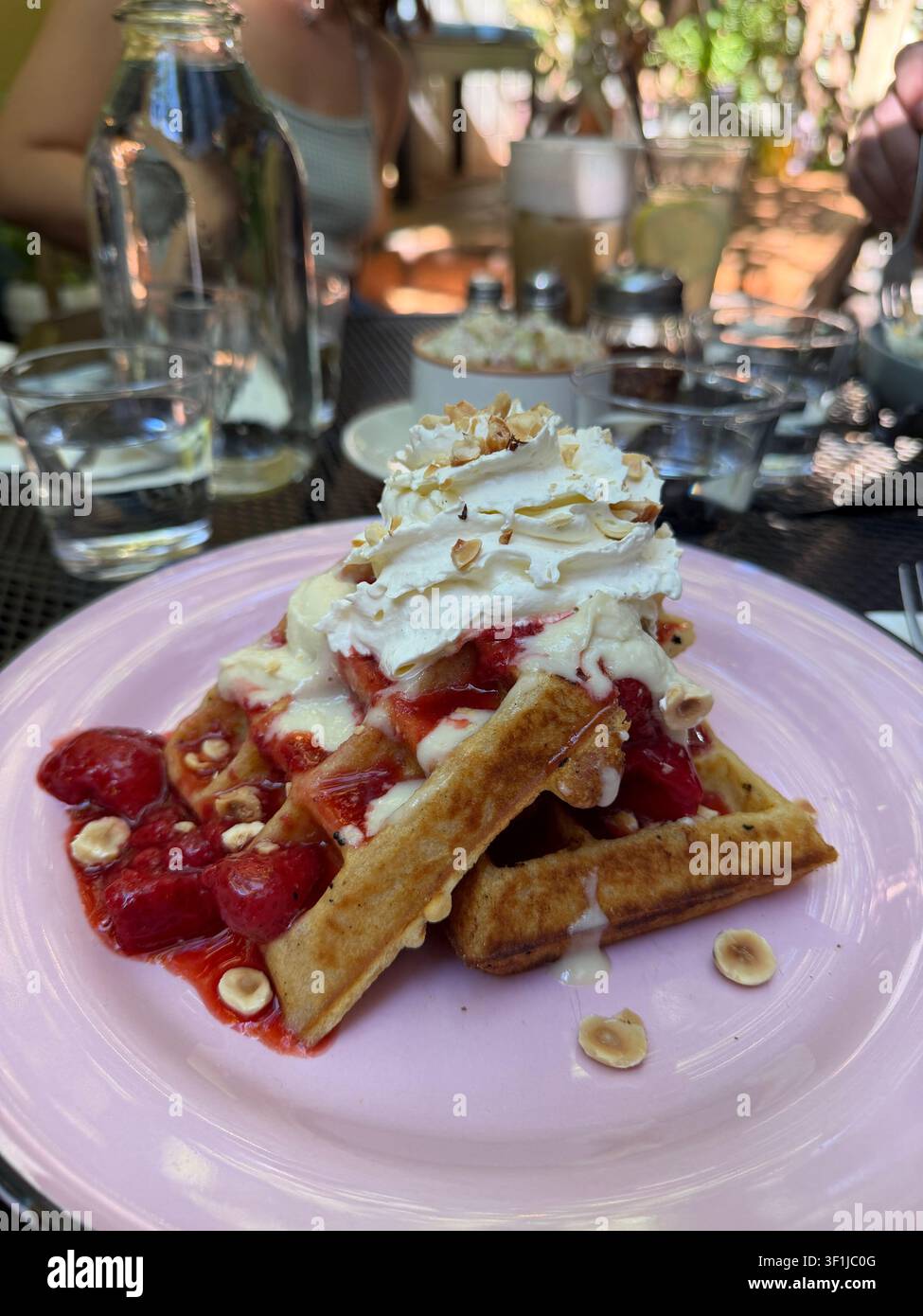 Gaufre belgiche con fragole e panna, su un piatto rosa a un tavolo in un caffè. Foto Stock