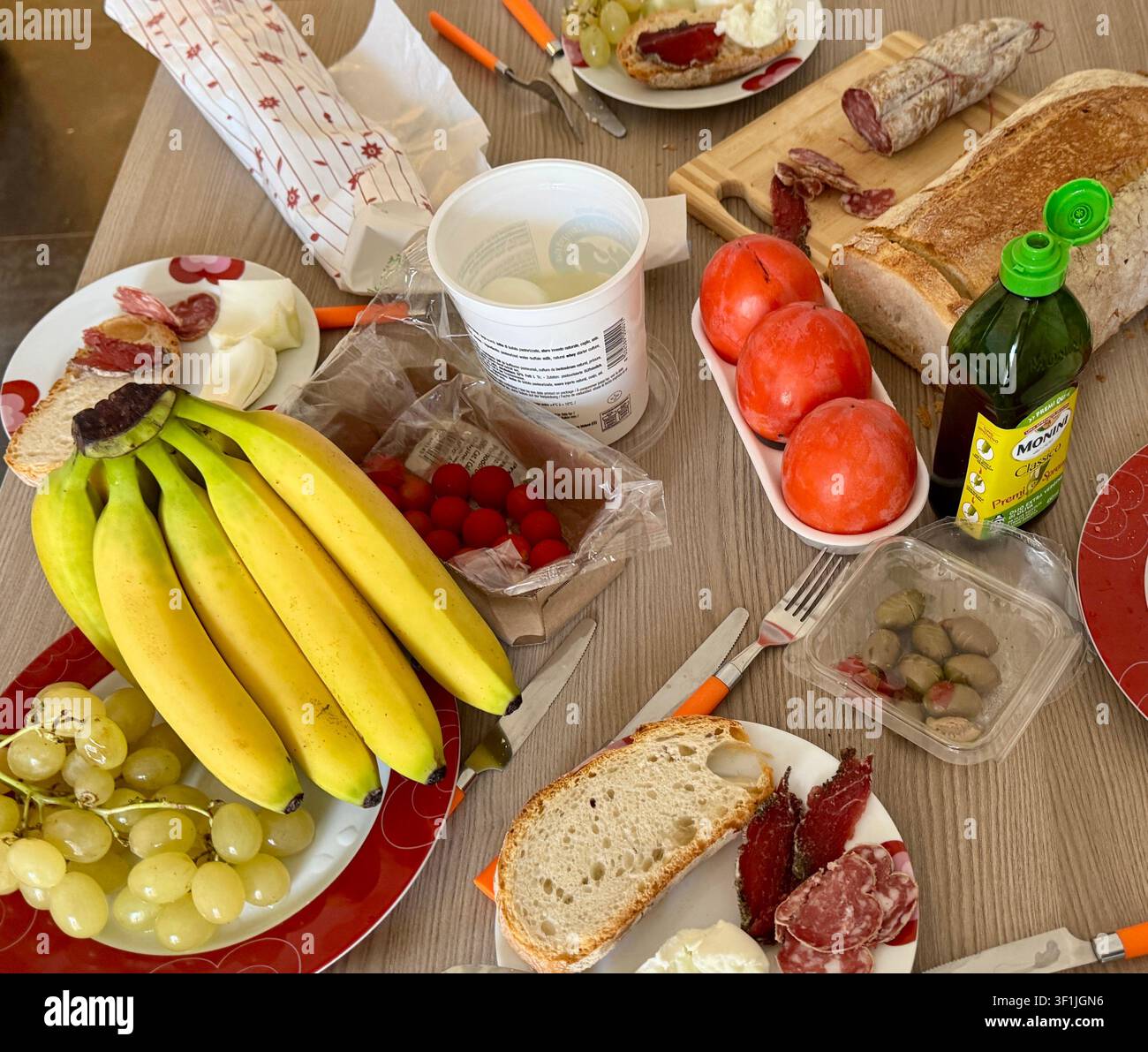 Tavolo apparecchiato con banane, uva, olive, pane, salame e cachi Foto Stock