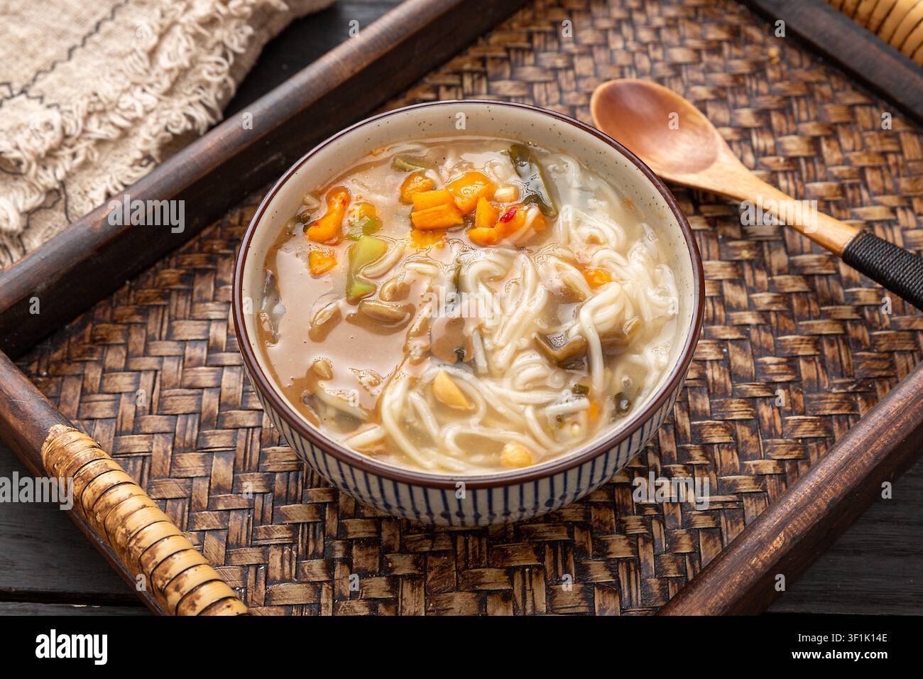 Nudli tradizionali cinesi Henan Fenjiang in zuppa di latte di soia fermentato, guarniti con arachidi, verdure e germogli di soia, serviti in una ciotola di ceramica. Foto Stock