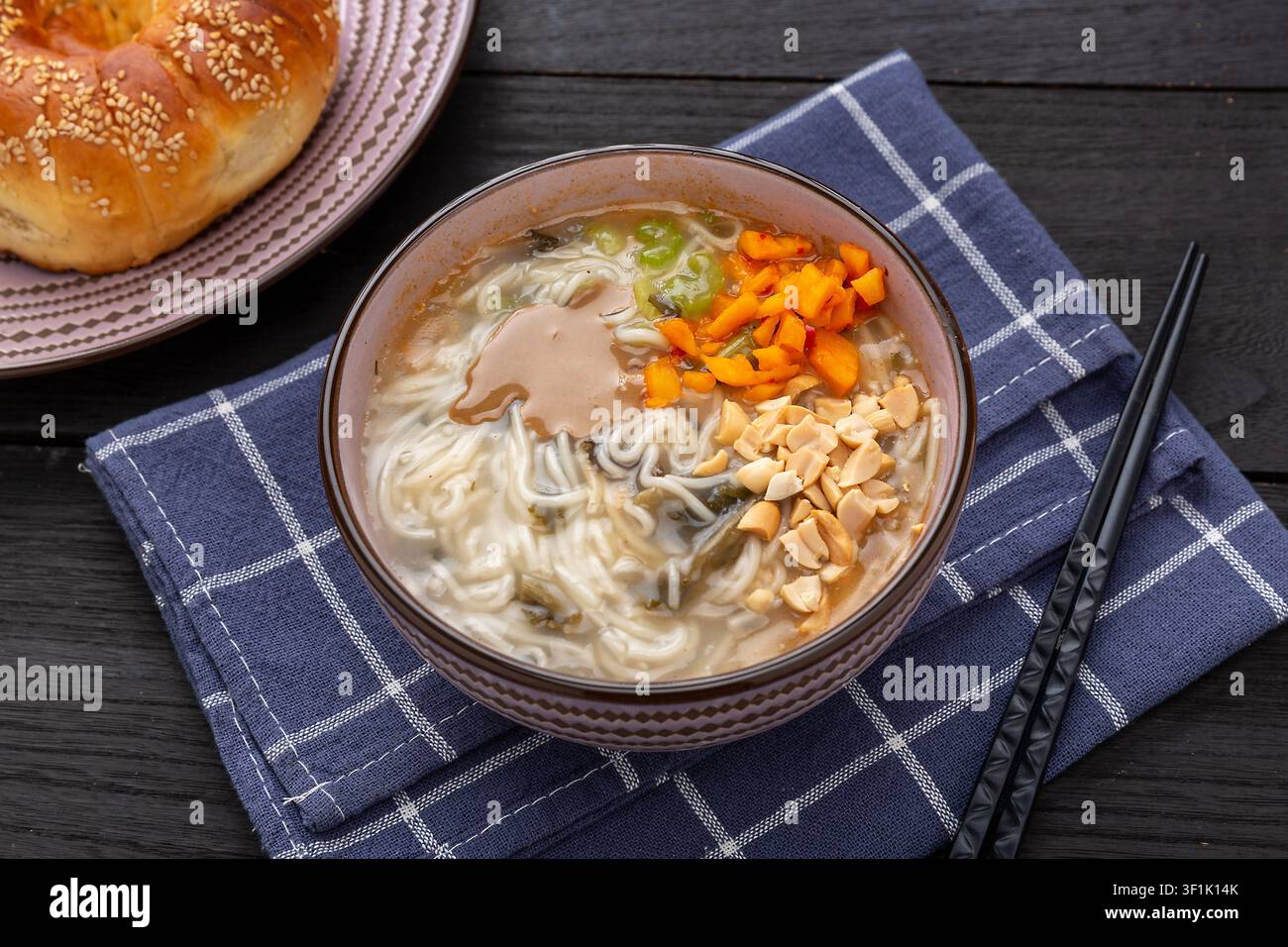 Nudli tradizionali cinesi Henan Fenjiang in zuppa di latte di soia fermentato, guarniti con arachidi, verdure e germogli di soia, serviti in una ciotola di ceramica. Foto Stock