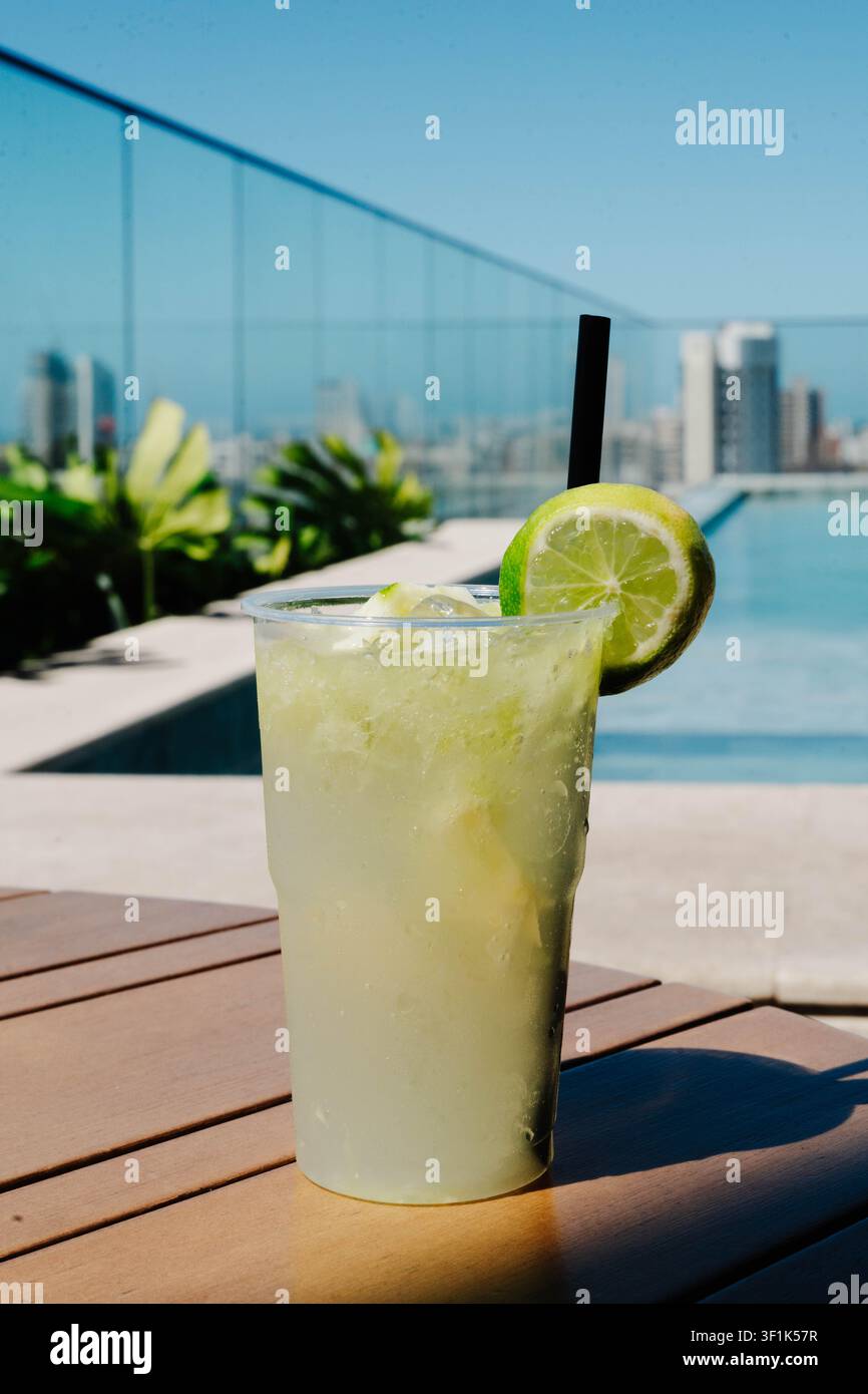 Cocktail caipirinha fresco servito in piscina sul tetto con lo skyline della città sullo sfondo. I cocktail stagionali celebrano i viaggi estivi, i sapori locali e Foto Stock