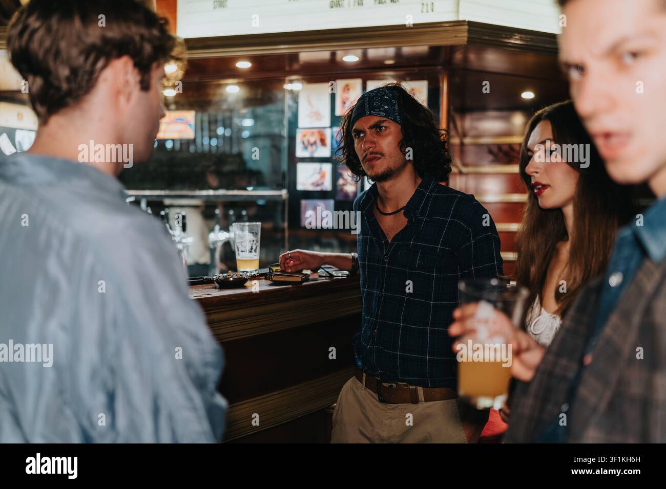 Amici che hanno una conversazione tesa in un bar mentre tengono birre e sono in piedi al bancone Foto Stock