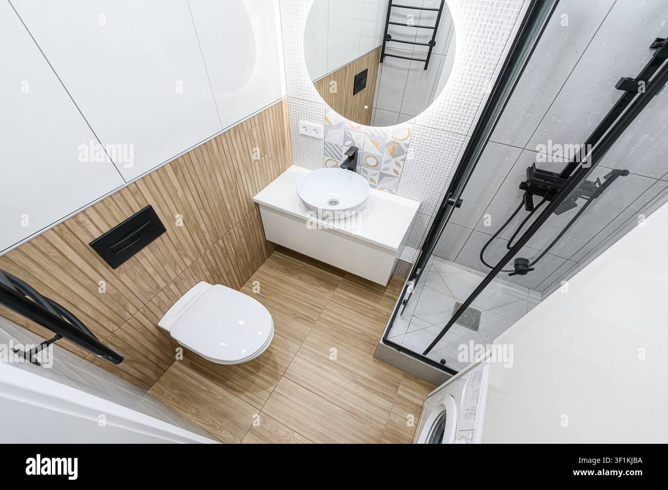 Bagno moderno. Palette di colori neutri, con piastrelle geometriche, dettagli in legno, specchio rotondo, toilette, doccia e lavandino bianco. Foto Stock