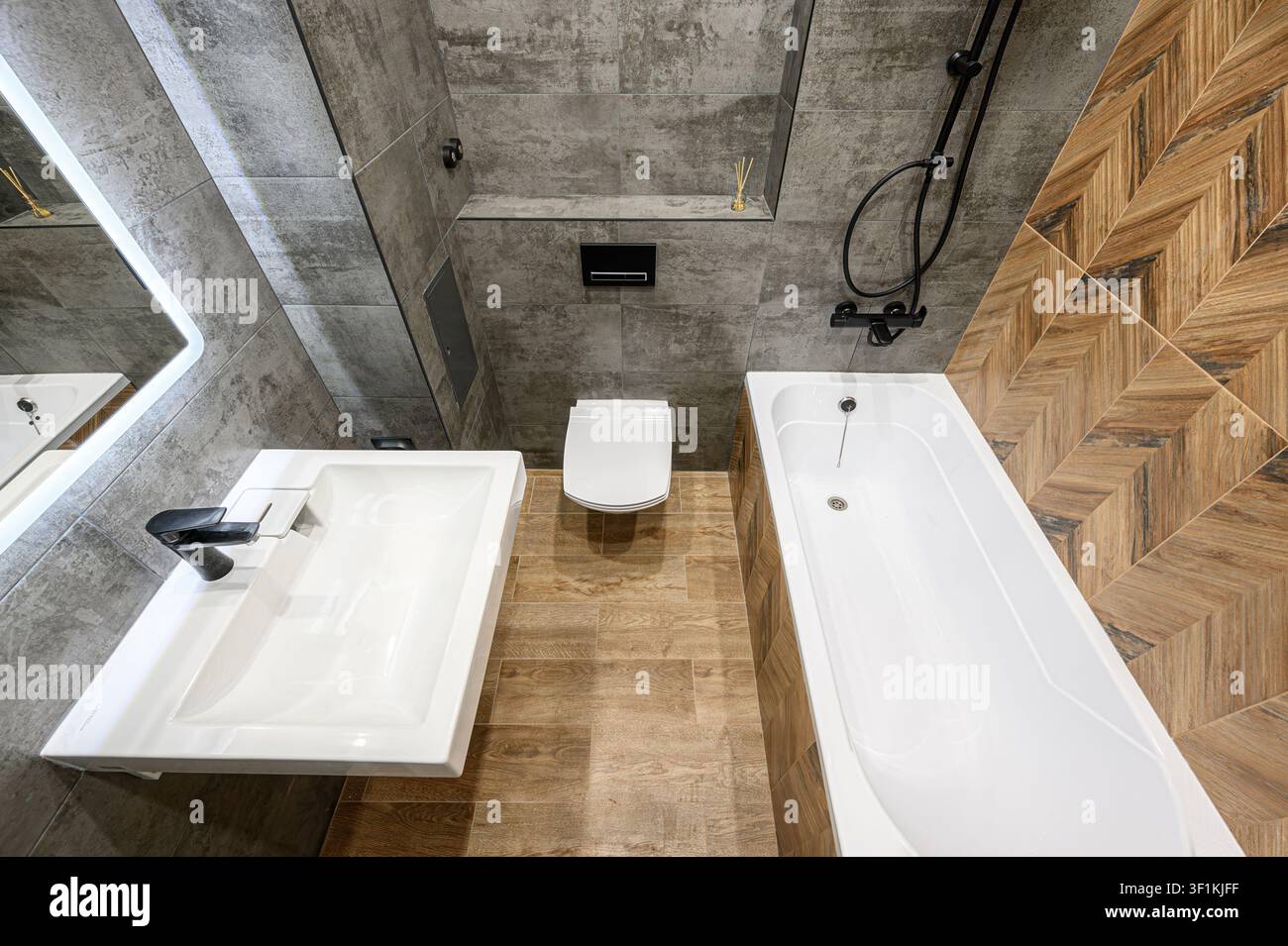 bagno moderno con piastrelle grigie, pavimento effetto legno e dettagli alle pareti, dotato di lavandino, WC e vasca da bagno Foto Stock
