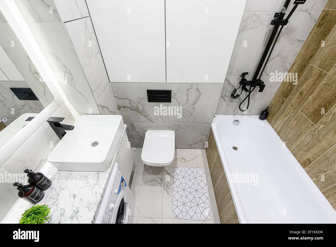 Bagno moderno con piastrelle in marmo bianco, un lavandino quadrato, toilette, vasca da bagno con set doccia nero e lavatrice Foto Stock