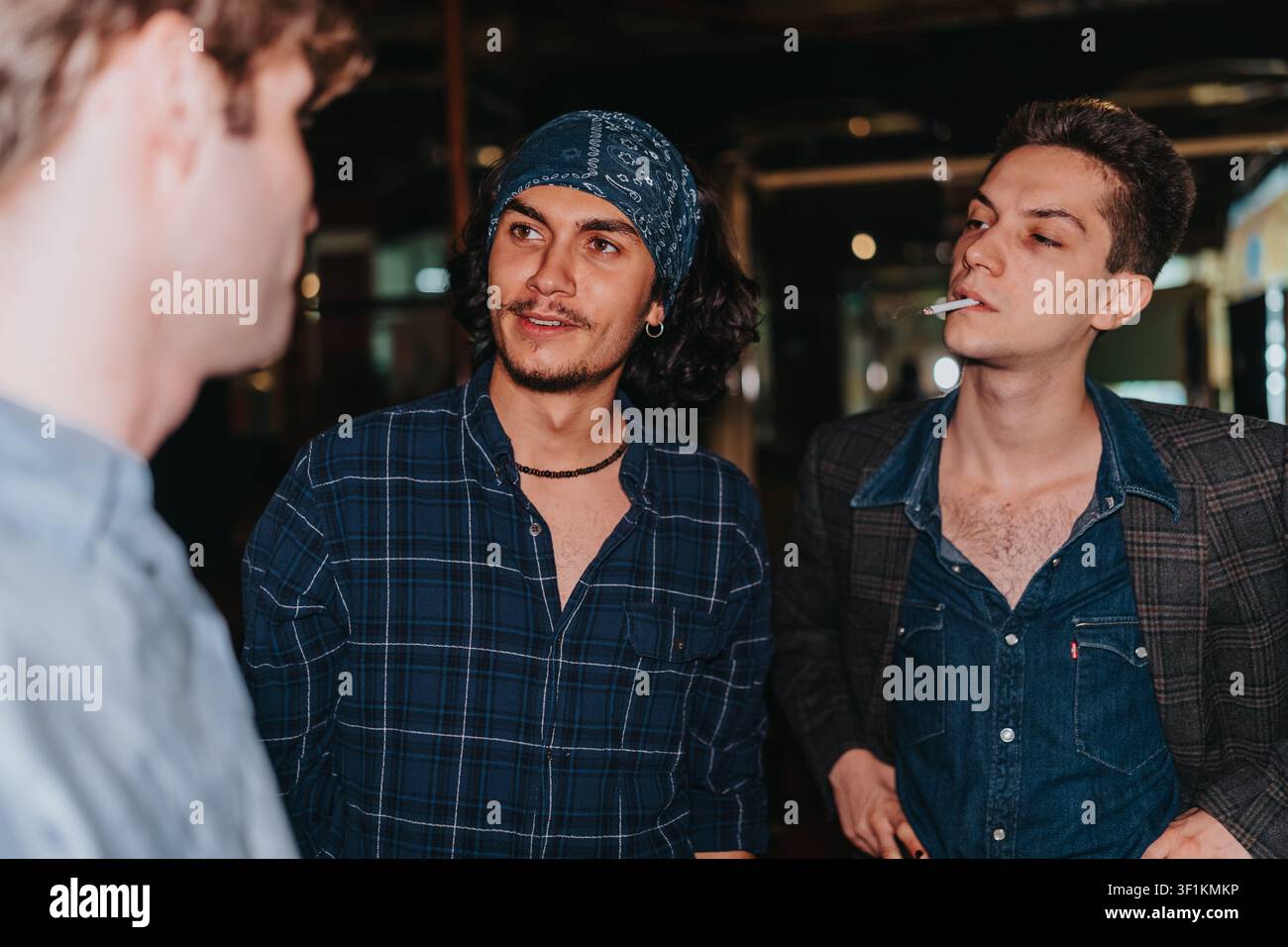 Tre amici che conversano in modo informale di notte, con un uomo che fuma una sigaretta Foto Stock