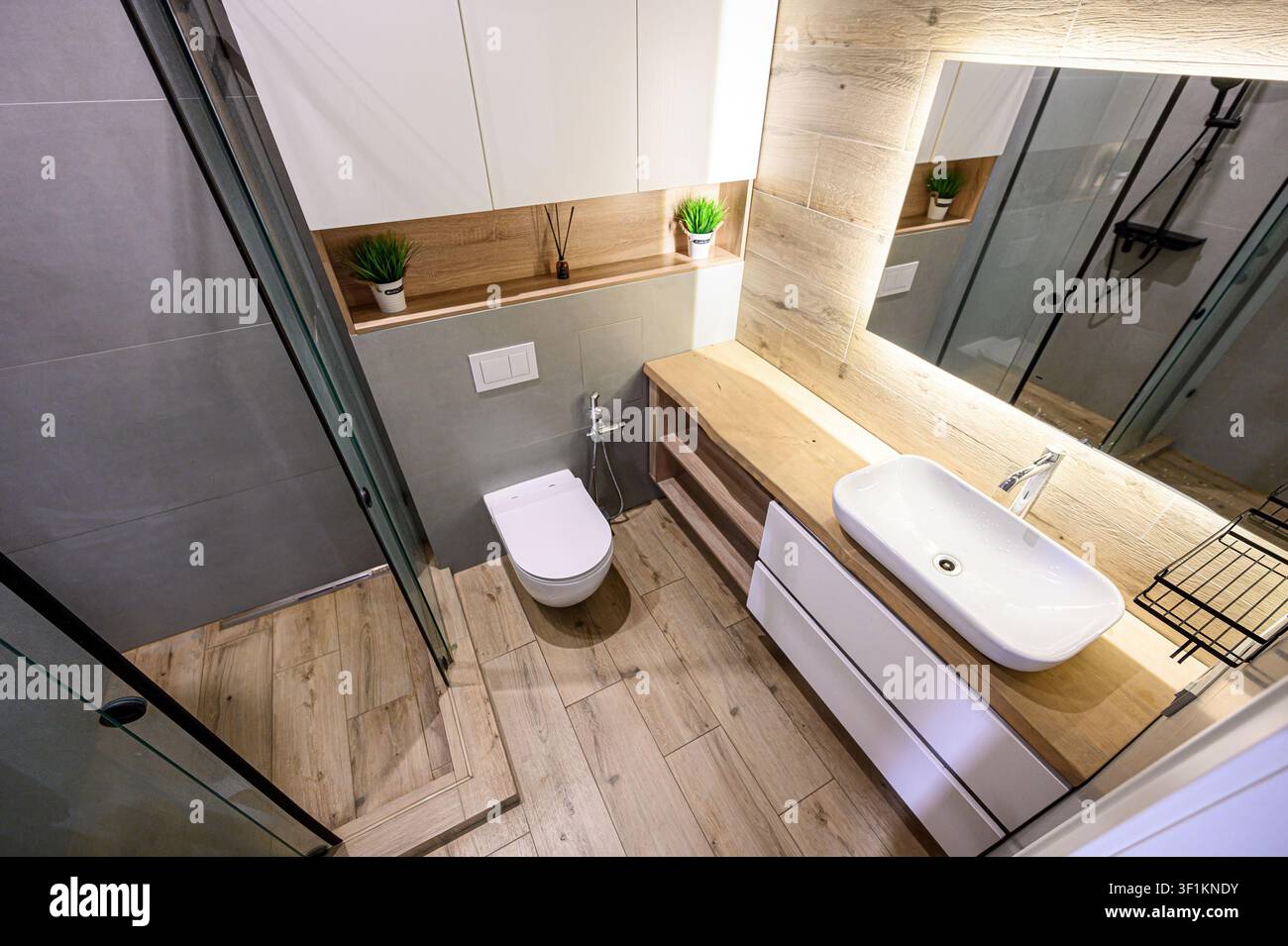bagno moderno con doccia in vetro, toilette, dettagli in legno e mobili bianchi Foto Stock