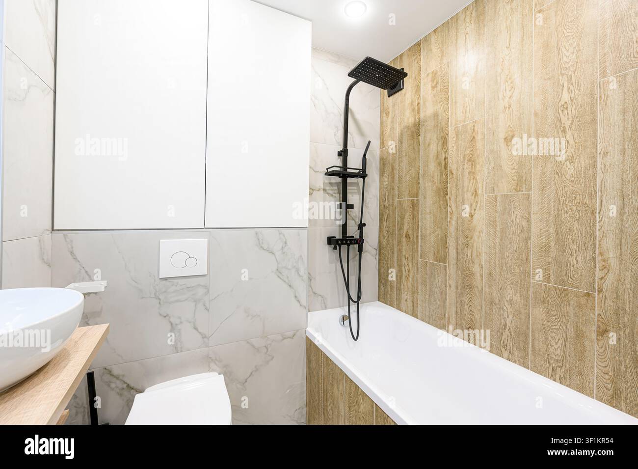 Bagno moderno con vasca bianca, rubinetto della doccia nero, piastrelle a motivi marmorizzati e dettagli in legno chiaro Foto Stock