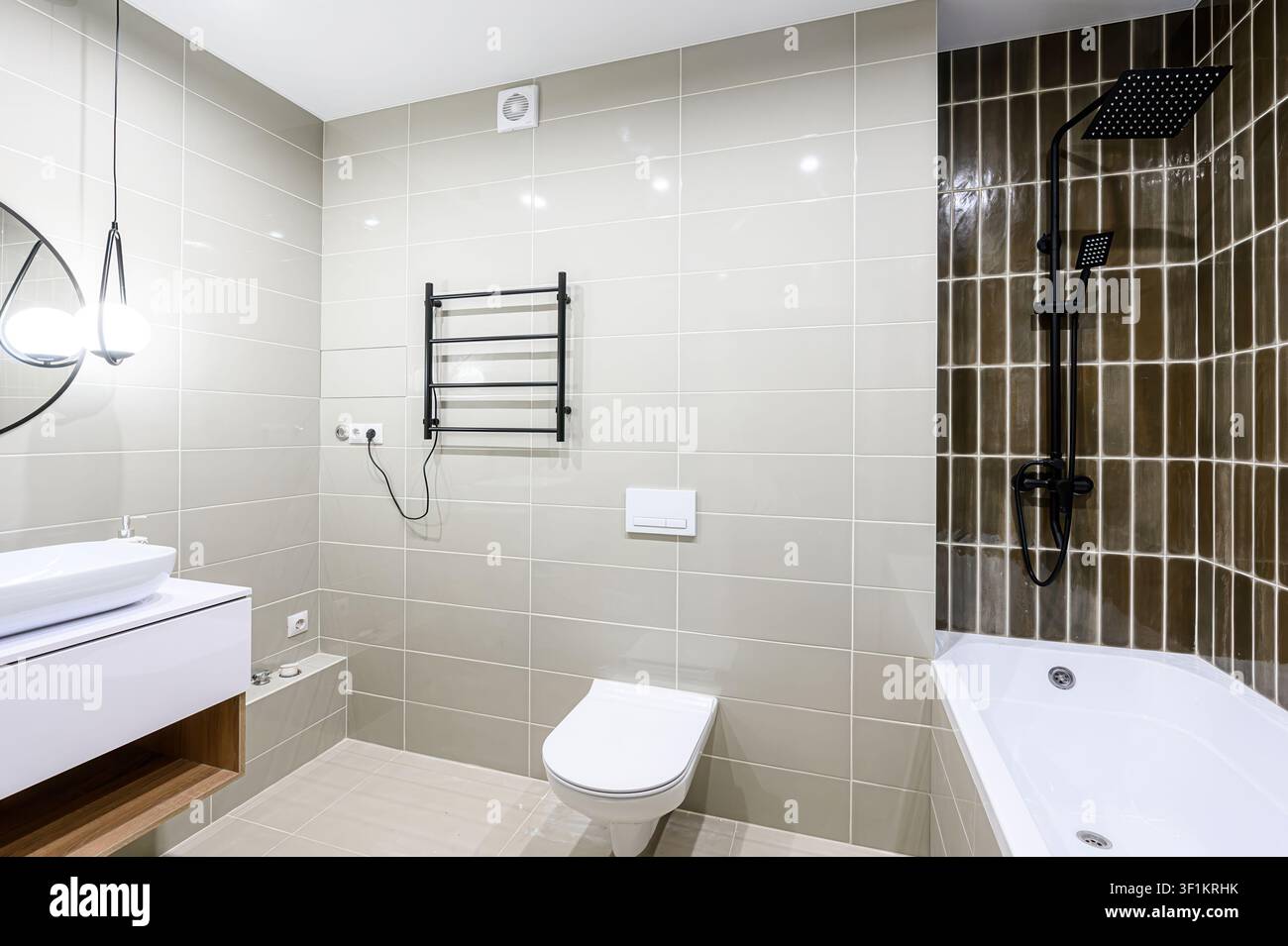 bagno moderno con piastrelle grigie, sanitari bianchi (toilette, lavandino, vasca) e dettagli neri nel portasciugamani e nella doccia. Lampade a sospensione sono appese sopra il Foto Stock