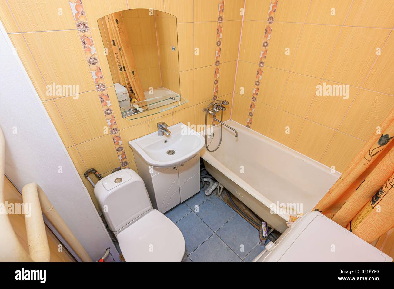 Bagno accogliente con piastrelle gialle, un lavandino bianco, toilette e vasca da bagno. Una tenda da doccia e uno specchio aggiungono dettagli allo spazio compatto Foto Stock
