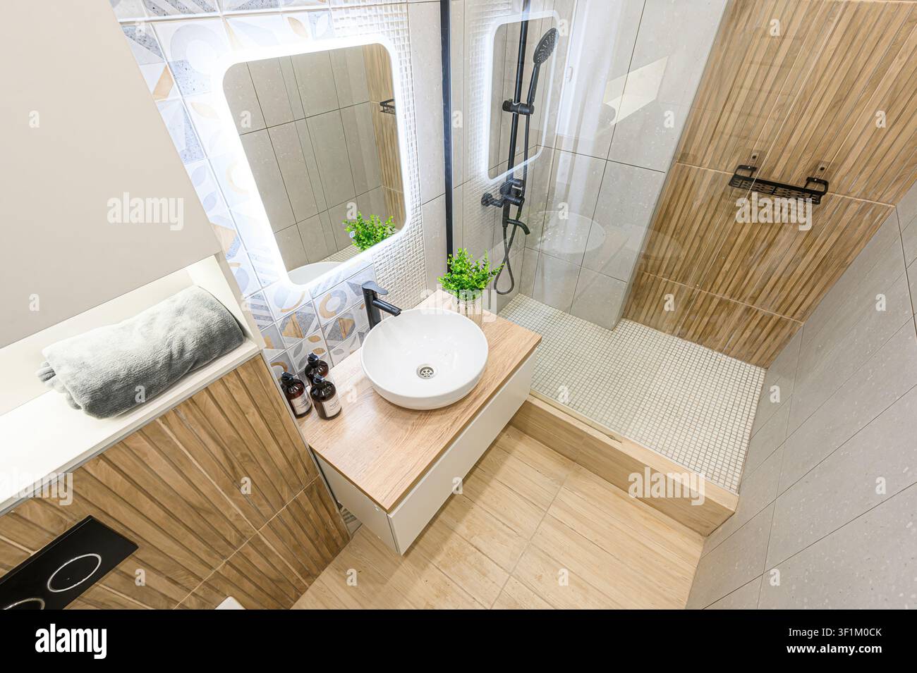 Bagno moderno con lavandino, specchio LED, doccia e dettagli in legno. Il design è pulito ed elegante Foto Stock
