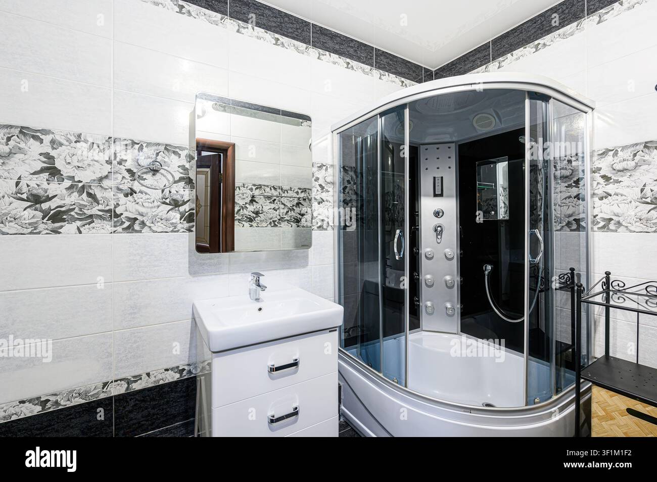 Bagno con pareti piastrellate, dettagli floreali, un lavandino bianco e una doccia vetrata Foto Stock