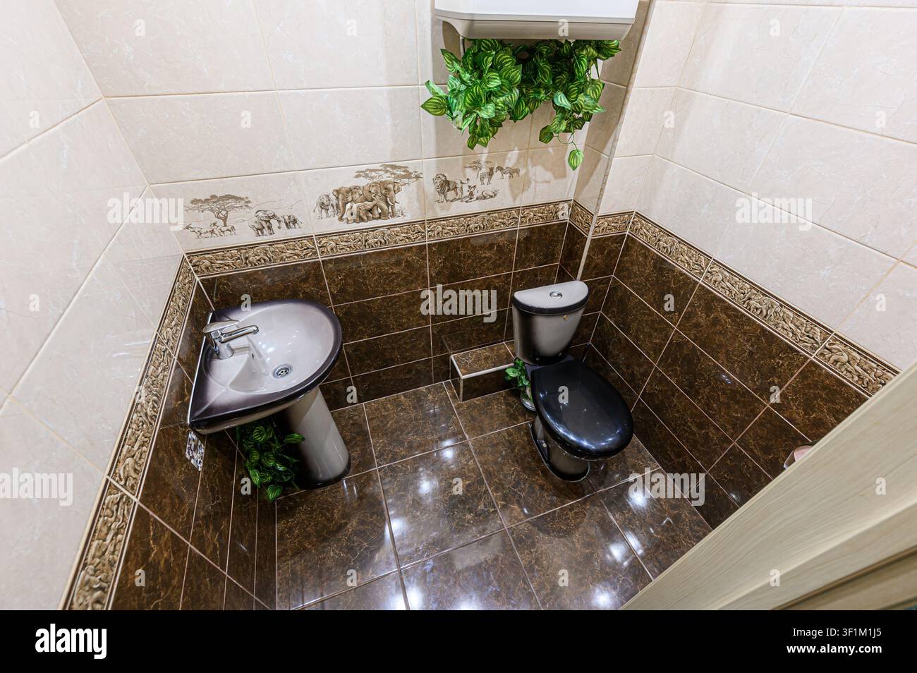 bagno con lavandino, toilette e decorazioni a fogliame. Le pareti sono in parte beige e marroni, con un design animale Foto Stock