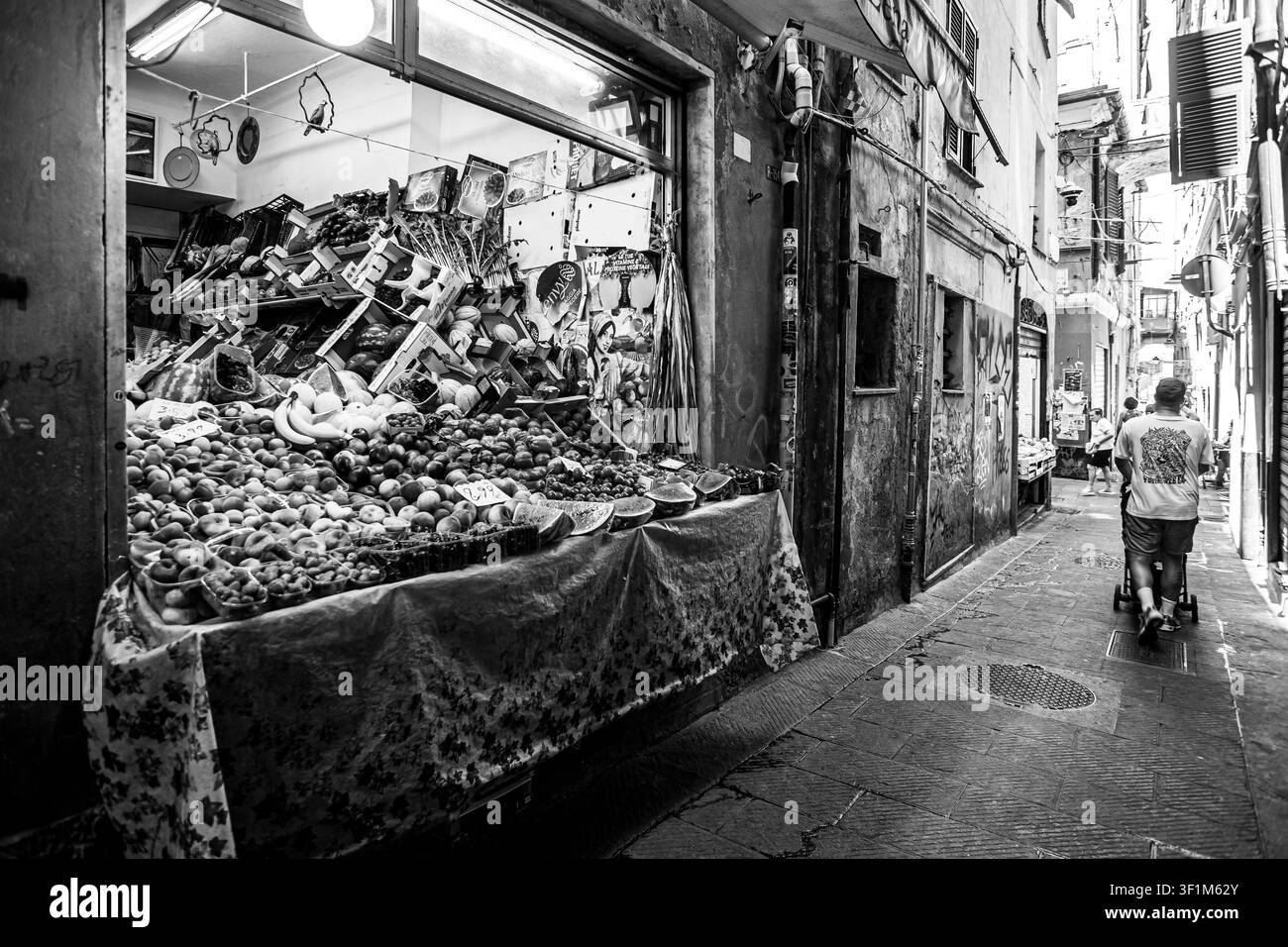 Italia Liguria Genova Italia, Liguria, Genova — Negozio di frutta e verdura nel centro storico di Genova, con prodotti colorati esposti all'esterno lungo le strette caruggi. Foto Stock