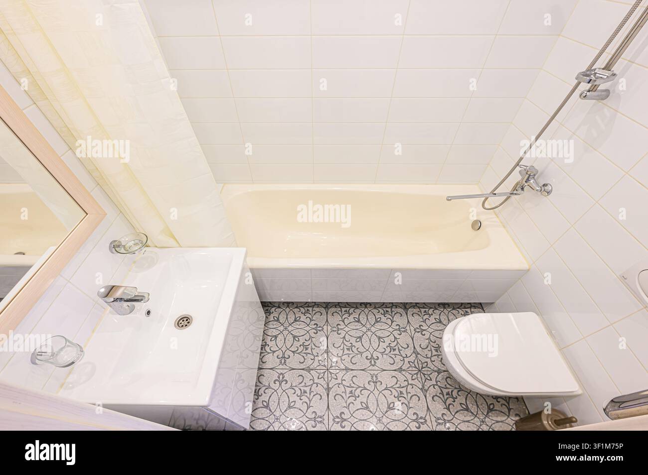 bagno luminoso con piastrelle bianche, una vasca color crema, un lavandino bianco e un pavimento a motivi Foto Stock
