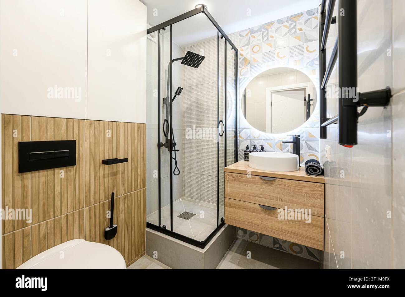 Bagno moderno con doccia con cornice nera, mobiletto con lavandino rotondo e piastrelle murali uniche. Accenti di nero sono presenti in tutto lo spa Foto Stock