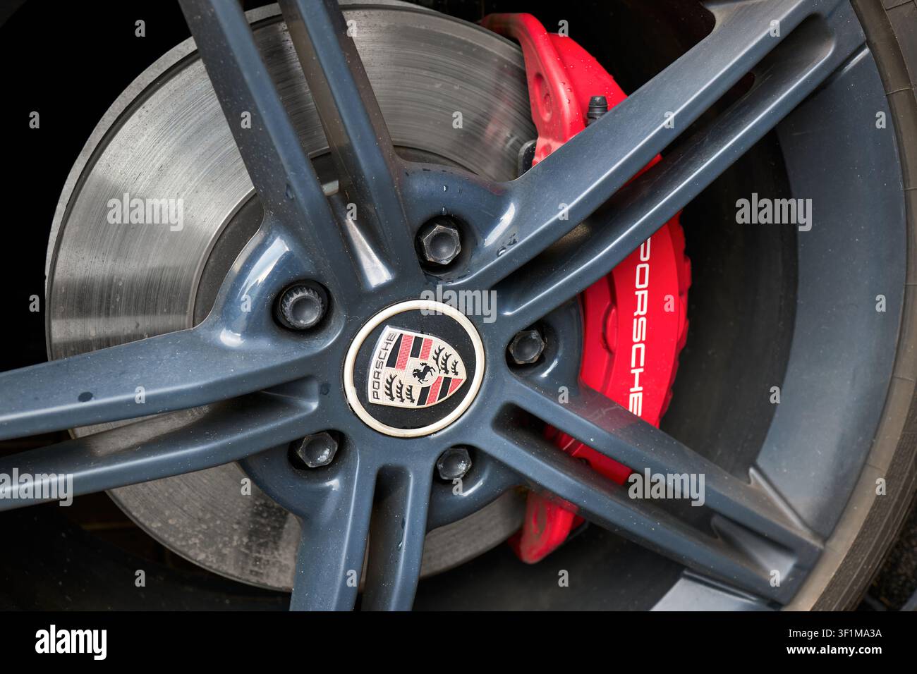 Primo piano di una ruota in lega grigia Porsche con pinza del freno rossa ben visibile, scritte bianche, logo iconico al centro e involucro in acciaio ventilato Foto Stock