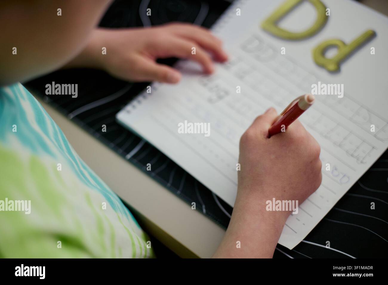 Primo piano di un bambino che pratica la calligrafia in un quaderno, tracciando lettere e sviluppando abilità di alfabetizzazione precoce. Utile per il marketing educativo, l'istruzione domestica, i programmi di lettura Foto Stock
