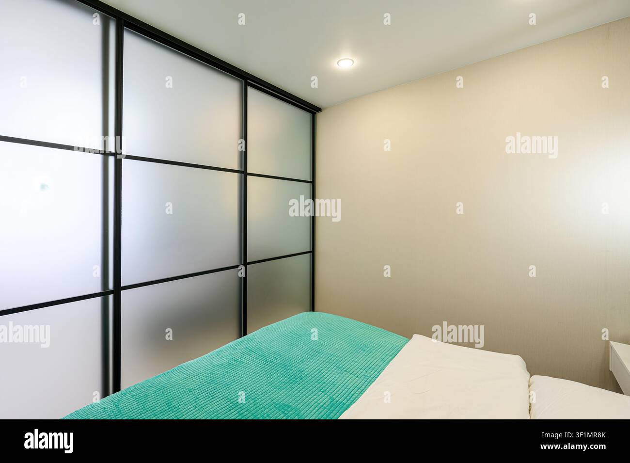 stanza moderna con letto con coperta turchese, lenzuola bianche e una parete in vetro satinato con cornici nere Foto Stock