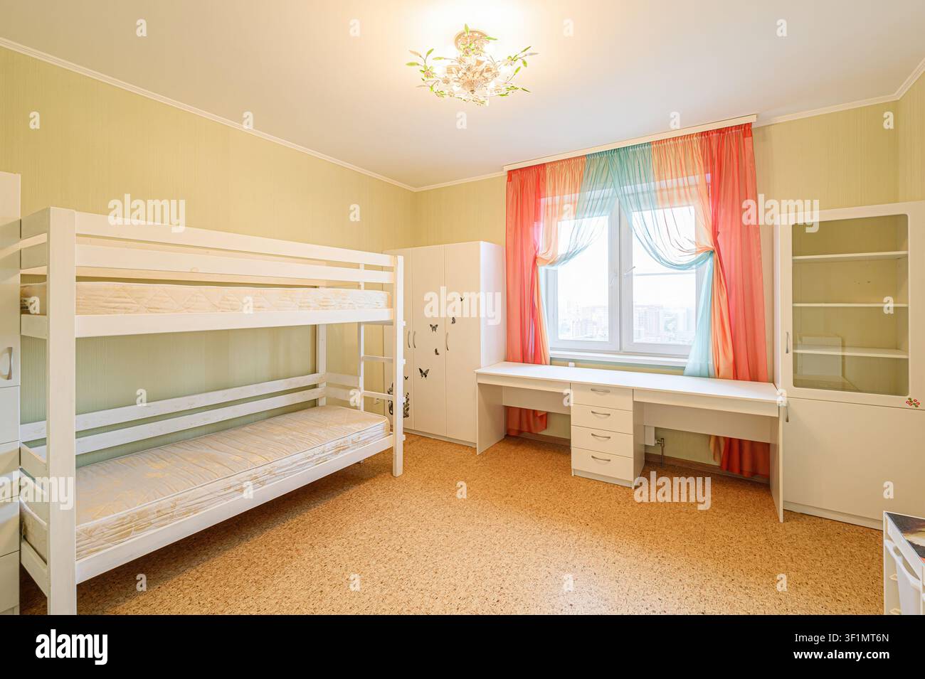 camera da letto accogliente con un letto a castello bianco, scrivania sotto la finestra con tende colorate, armadio e libreria Foto Stock