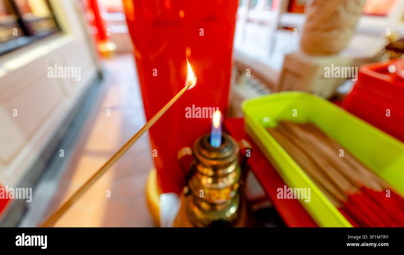 Un vivido primo piano di un bastoncino d'incenso acceso all'interno del Tempio Sunfong a Kaohsiung. La luce soffusa evidenzia l'atmosfera culturale e l'ambiente sacro di Foto Stock
