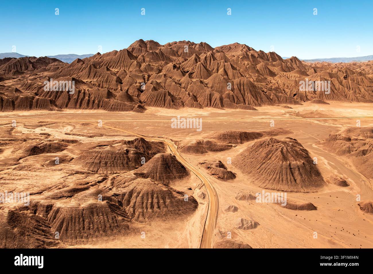 Panorama aereo di badlands erosi e formazioni terrestri frastagliate nel Desierto del Diablo, Salta, Argentina, con pianure sabbiose e una strada sterrata sinuosa e Foto Stock