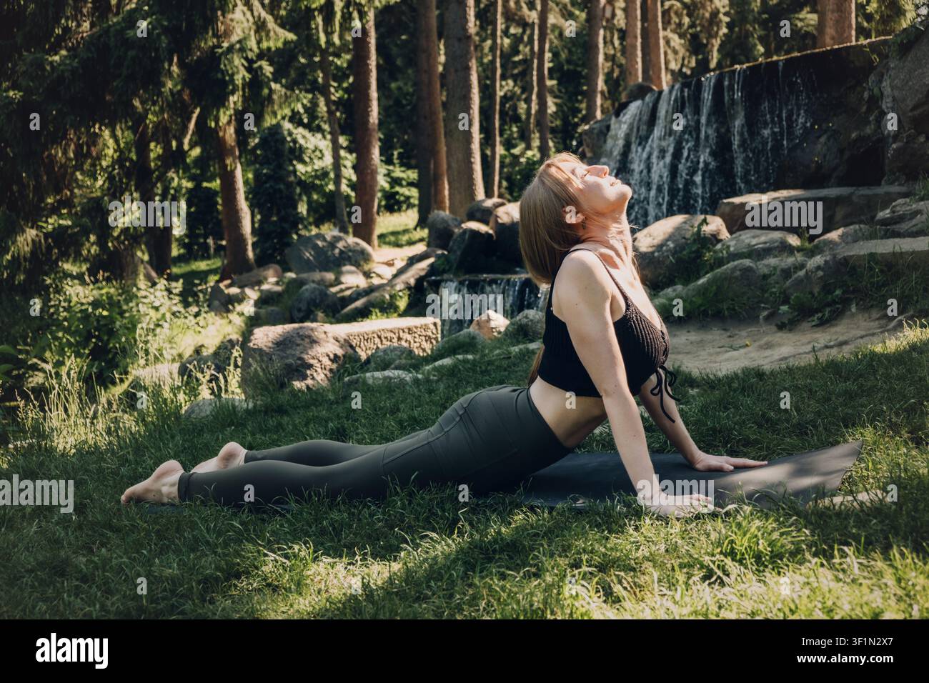 Giovane donna adulta esegue la posa del cobra su un tappeto all'aperto. Yoga mattutino energizzante, esercizi di allungamento per il sollievo dal dolore alla schiena, movimenti per il rafforzamento del tronco, all'aperto Foto Stock