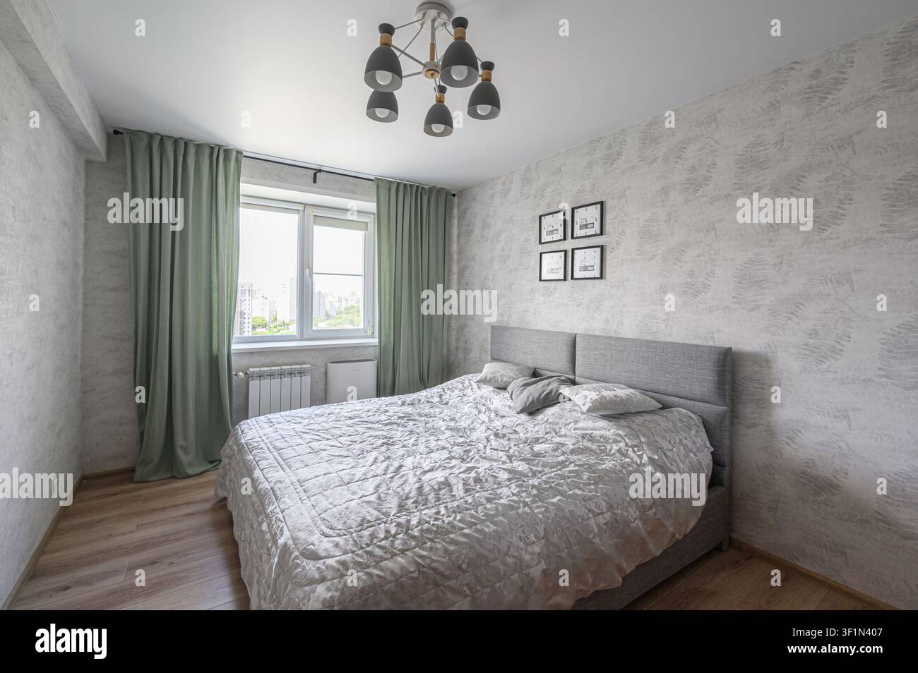 Camera da letto accogliente con un letto grigio, carta da parati a motivi e tende verdi morbide vicino a una finestra. Lampadario moderno sospeso Foto Stock