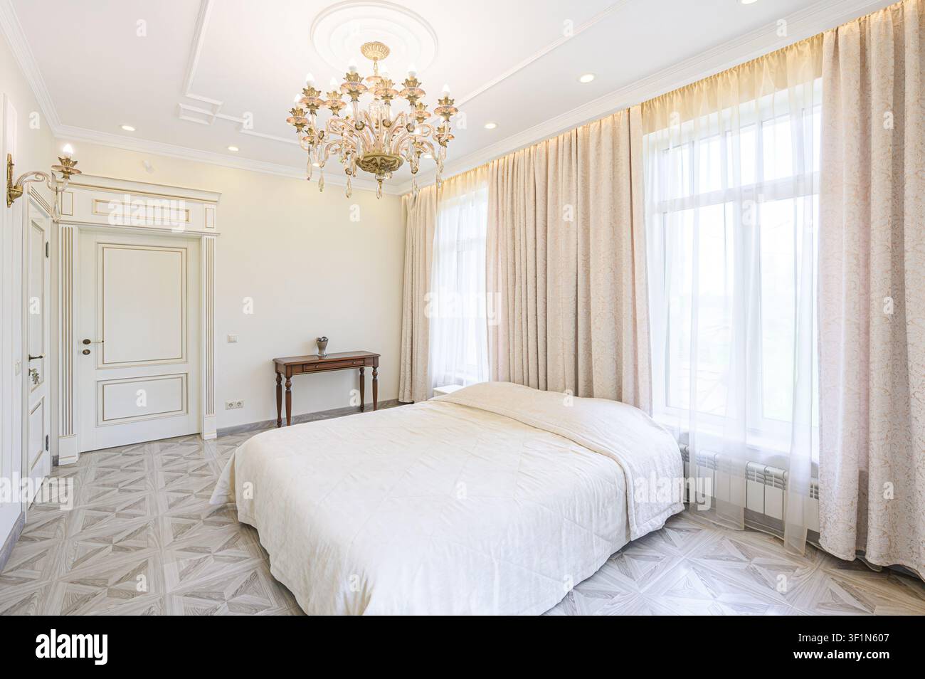 Camera da letto elegante con lenzuola bianche, tende leggere, un lampadario di cristallo e pavimentazione a motivi Foto Stock