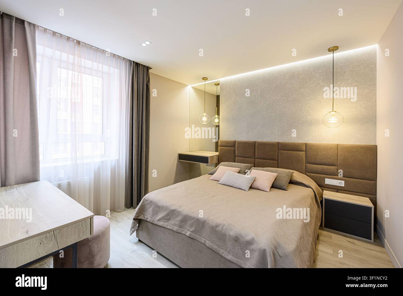 camera da letto accogliente con un letto grande, illuminazione soffusa e colori neutri, che crea un'atmosfera rilassante Foto Stock