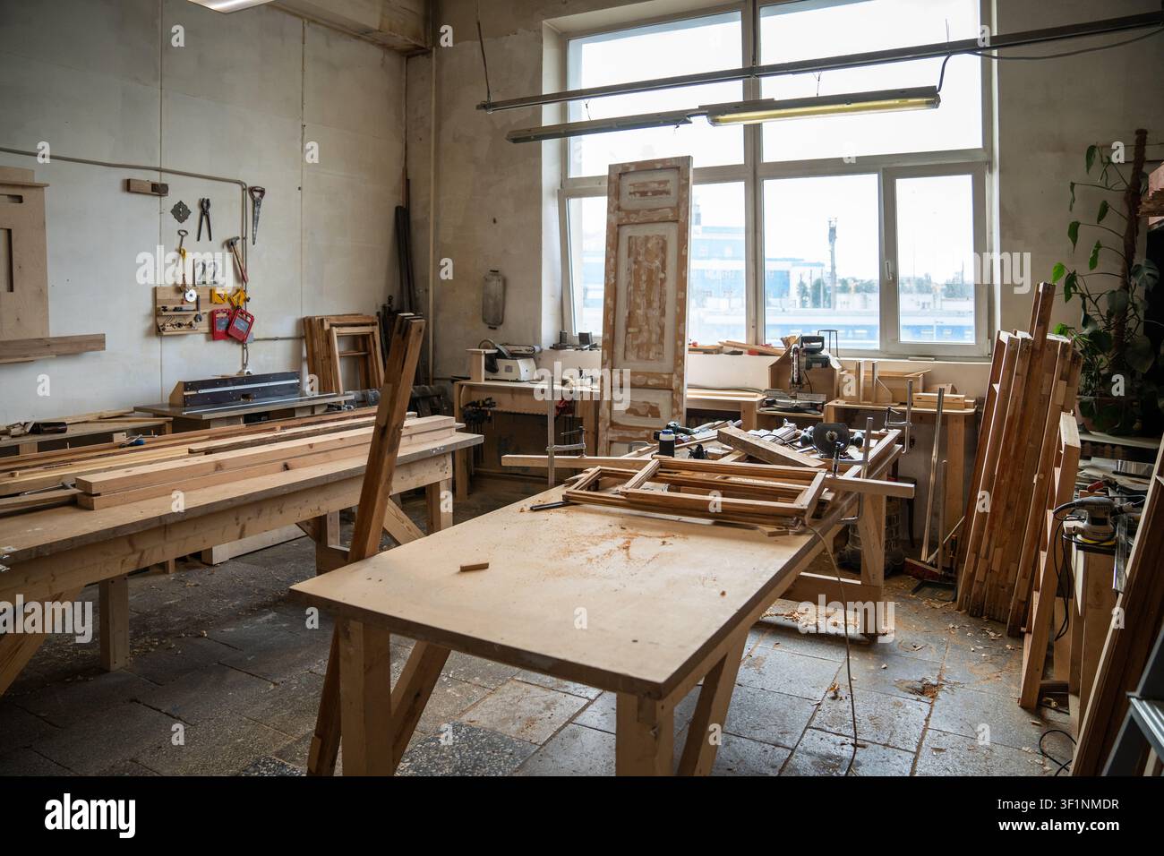 Ampio interno di officina di restauro organizzato con tavolo da lavoro, strumenti, attrezzi e finestra. Foto Stock