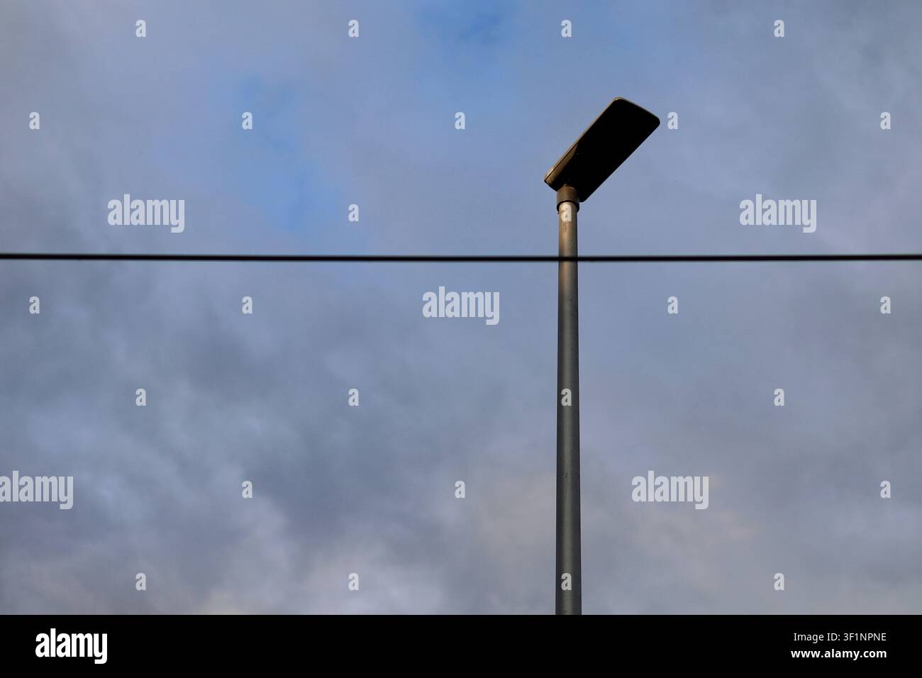 Lampione minimalista contro un cielo nuvoloso drammatico con cavo sospeso e infrastrutture urbane Foto Stock