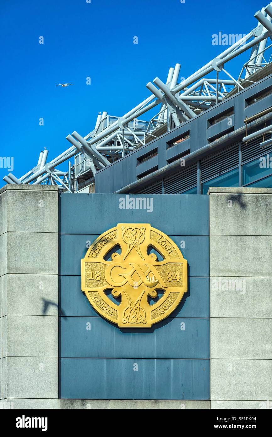 Emblema del logo della croce celtica GAA dorata sulla facciata in cemento dello stadio Croke Park a Dublino in una giornata di sole. Foto Stock