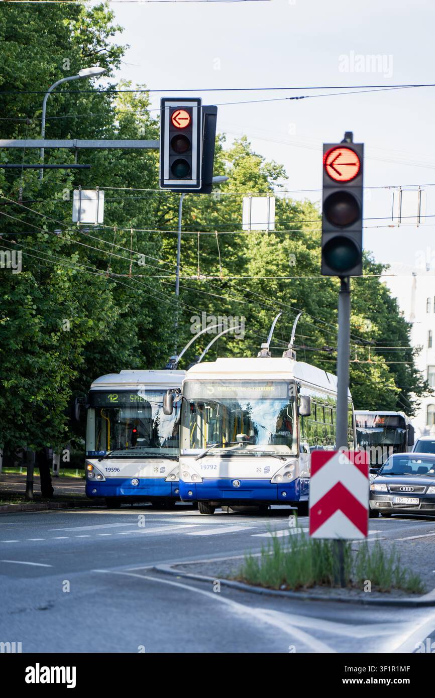 Autobus elettrici sostenibili per il trasporto pubblico municipale che eseguono percorsi sotto cavi di servizio aerei e segnali di traffico direzionali intelligenti Foto Stock