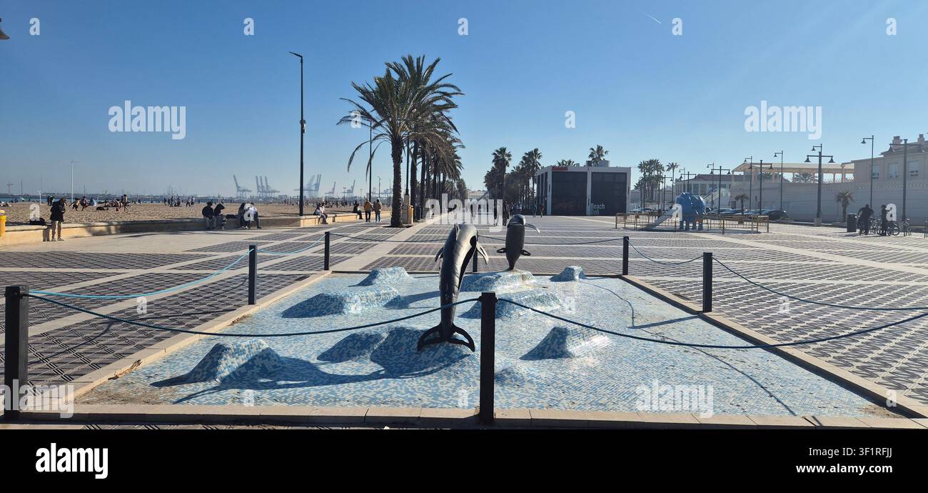 VALENCIA, SPAGNA - MARZO 2026: Vista ampia del lungomare di Malvarrosa con la scultura della fontana dei delfini e palme sotto un cielo azzurro. - Immagine stock catturata con smartphone