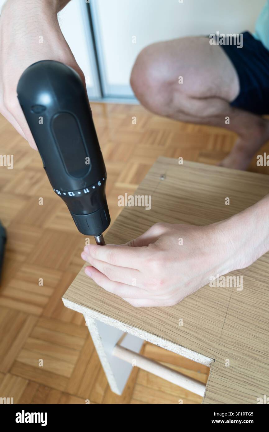 Primo piano di una avvitrice a batteria che fissa una vite in un pannello di legno di panchina durante il montaggio Foto Stock