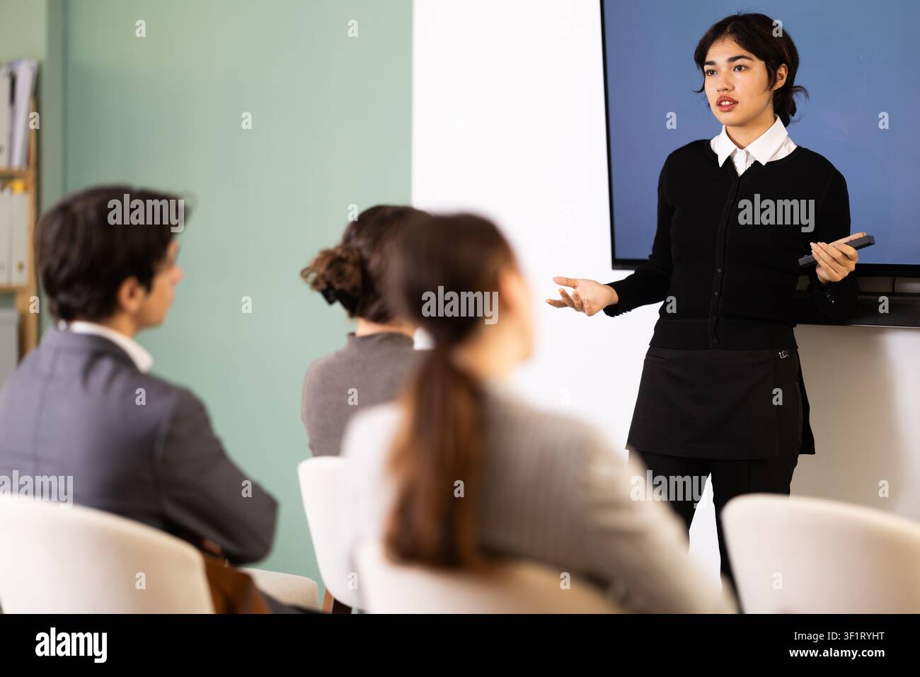 Giovane donna che presenta con telecomando nella sala riunioni Foto Stock