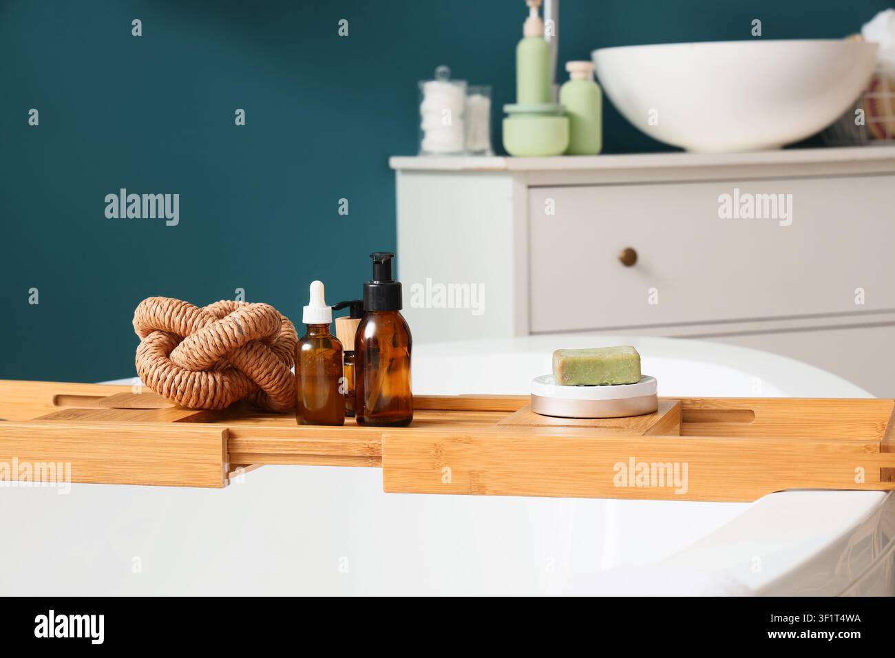 Porta-bagno in bambù con prodotti naturali per la cura della pelle e un nodo decorativo su una vasca da bagno bianca in un bagno moderno, un nodo intrecciato decorativo e una luffa Foto Stock