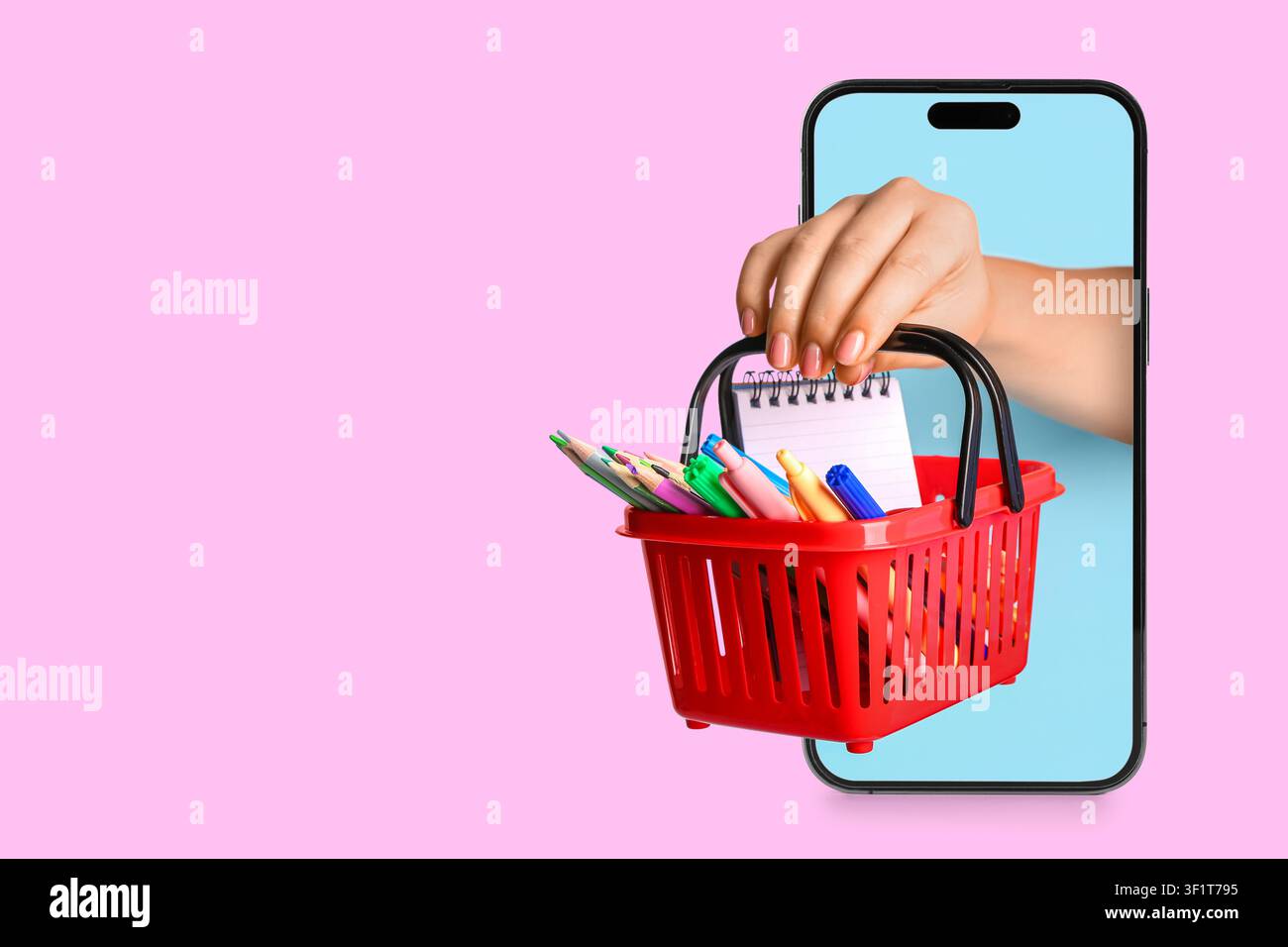 Mano che tiene un cestino della spesa rosso con materiale scolastico emergente dallo schermo di uno smartphone, istruzione online e ritorno a scuola Foto Stock