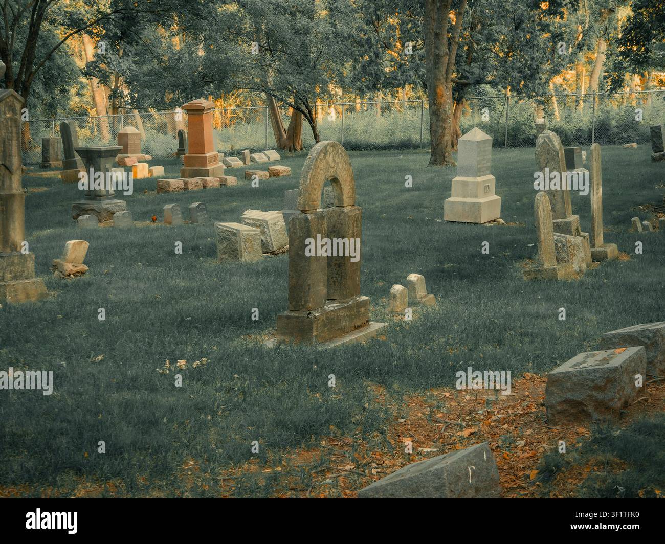 Una serie di lapidi e monumenti storici in un cimitero tranquillo e alberato al tramonto Foto Stock