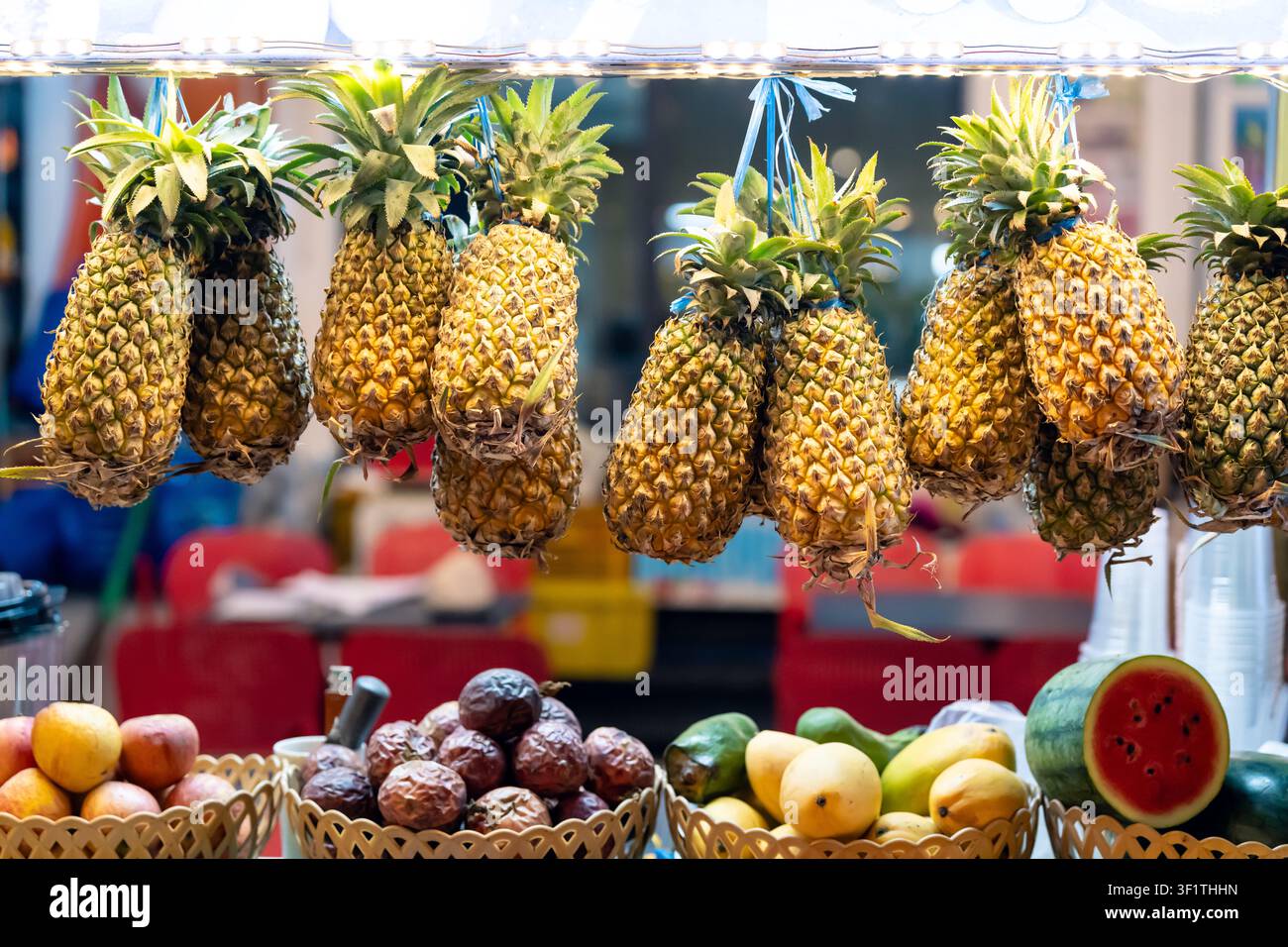Ananas appesi e frutti tropicali misti a un vivace banco di mercato a Phu Quoc in un ambiente luminoso Foto Stock