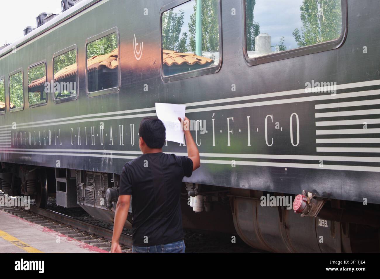 Agente di meet-and-greet che tiene un cartello di carta sopra la testa nella stazione ferroviaria di Creel con il vagone passeggeri del Chepe Express sullo sfondo. Creel Foto Stock