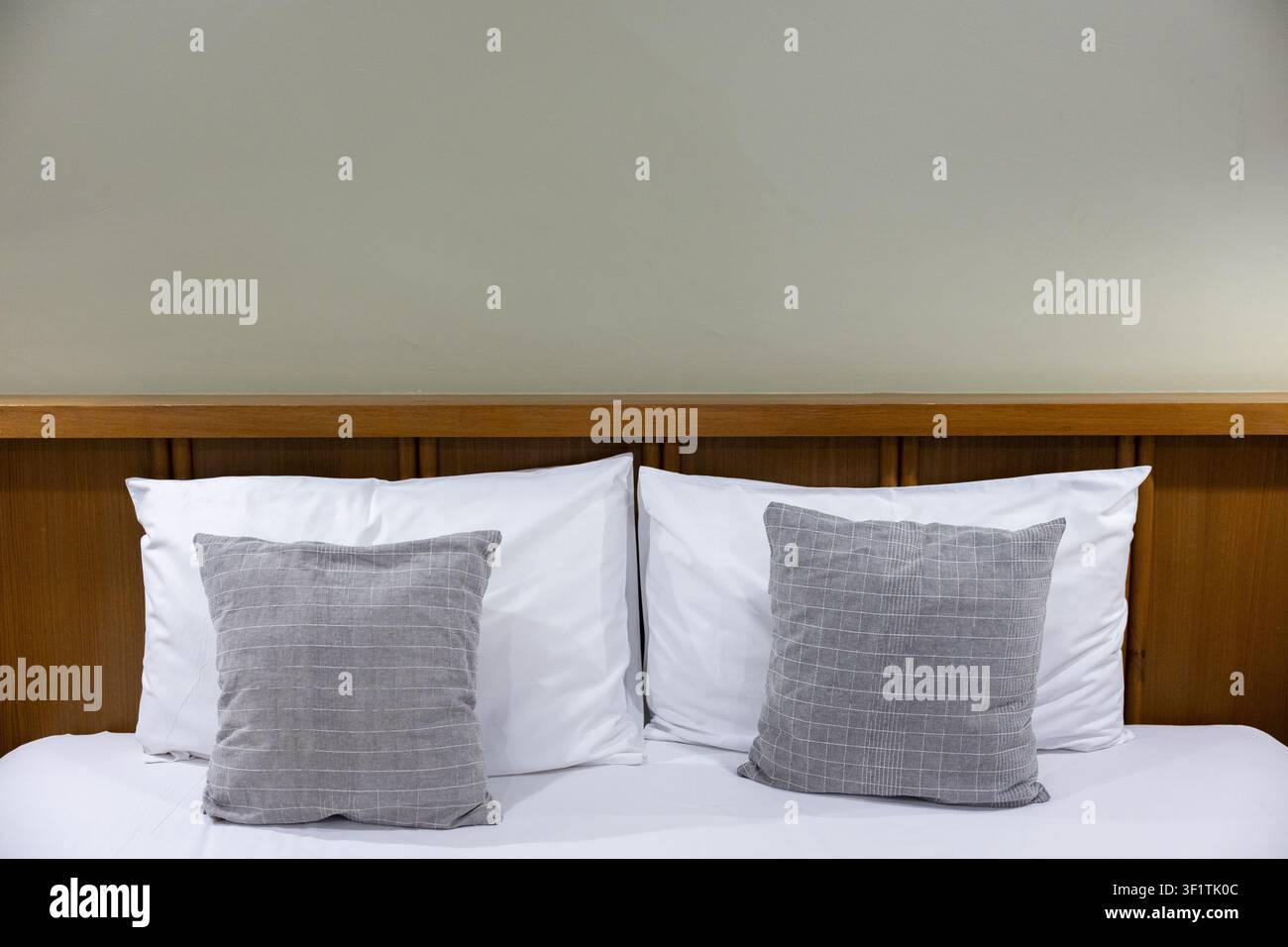 Due cuscini decorativi grigi su un letto bianco con testiera in legno, scena di camera da letto minimalista e accogliente che trasmette calma e comfort Foto Stock