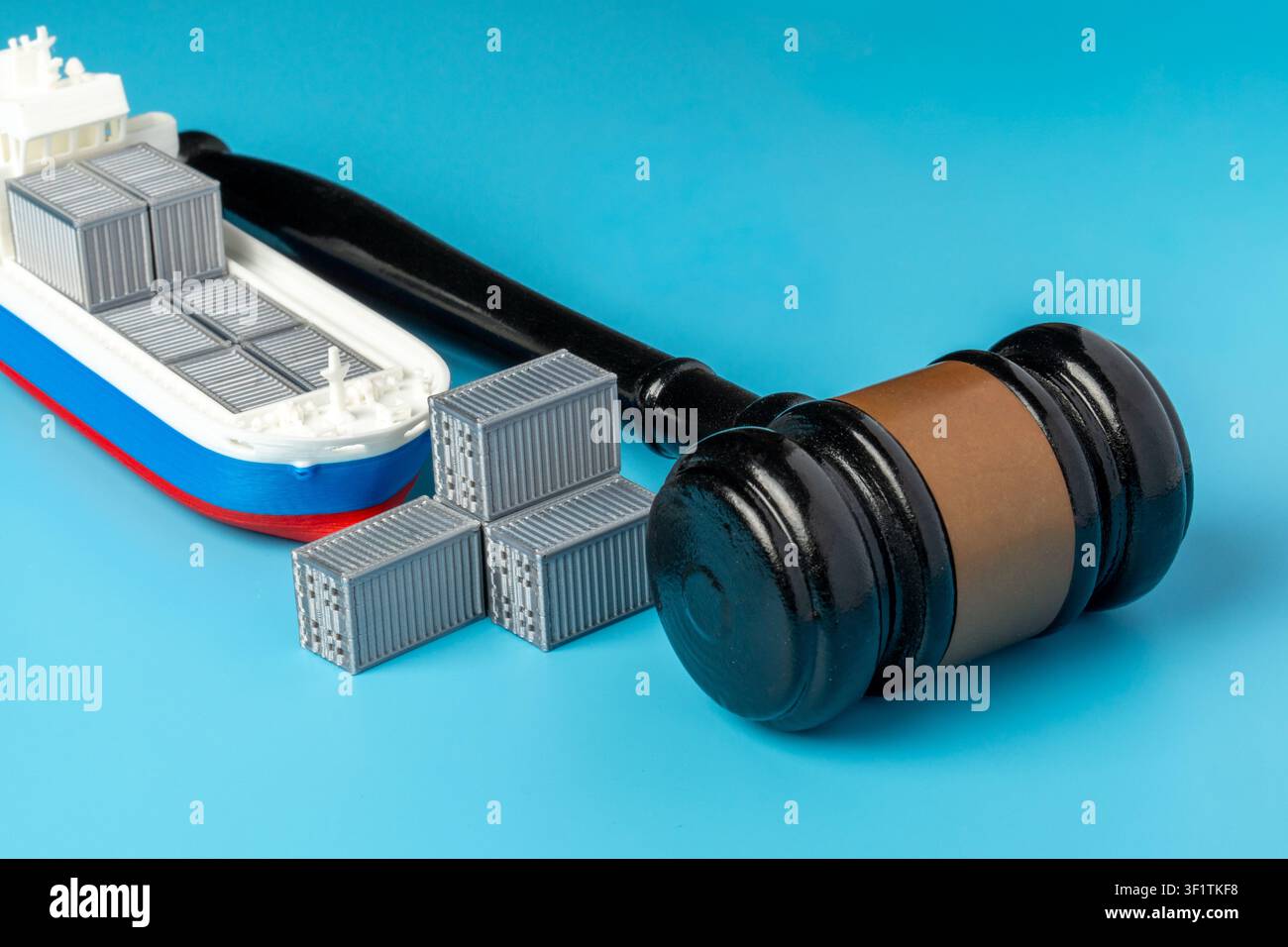 Miniatura di una nave da carico e un martelletto del giudice su sfondo blu. Diritto marittimo, regolamenti commerciali internazionali, dispute doganali, embarghi sulle spedizioni Foto Stock